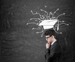 Man standing against a dark chalkboard and a graduation hat drawn right above his head